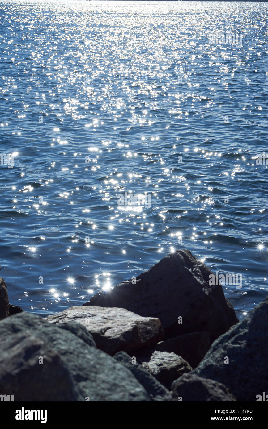 Steine und Felsen im Vordergrund der glitzernden Sonne auf dem Wasser Stockfoto