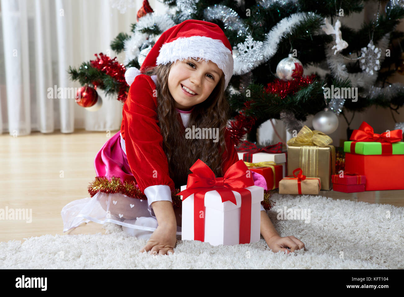 Feier von Weihnachten, Winter Urlaub und Personen Konzept. Glückliche junge Mädchen mit Geschenken in den Feldern in der Nähe eines geschmückten Weihnachtsbaum zu Hause sitzen Stockfoto