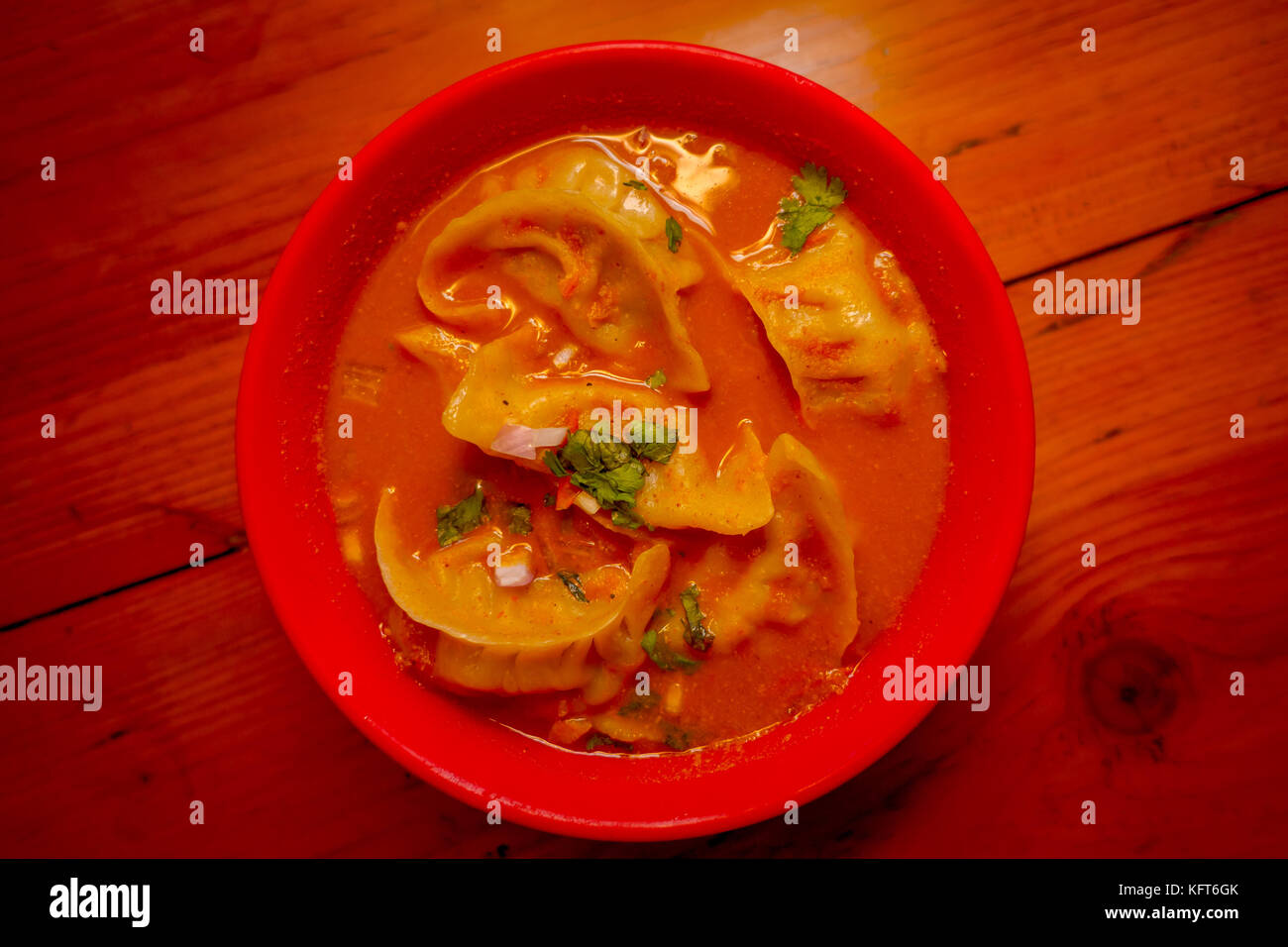 Blick von oben auf die gedämpfte Suppe von Momo in einer roten Schüssel serviert. Ein beliebtes Nepalesisches Essen, die auch im Val di Chiana, Bhutan, Tibet und Indien üblich ist, in einem hölzernen Tisch Hintergrund Stockfoto