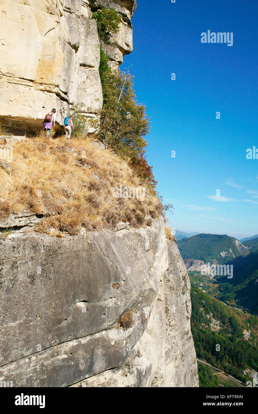 LUFTAUFNAHME. Zwei junge Frauen wandern auf einem Weg „in den Himmel“ unter dem wachsamen Auge des Sandsteinhüters. ANNOT, Alpes-de-Haute-Provence, Frankreich. Stockfoto