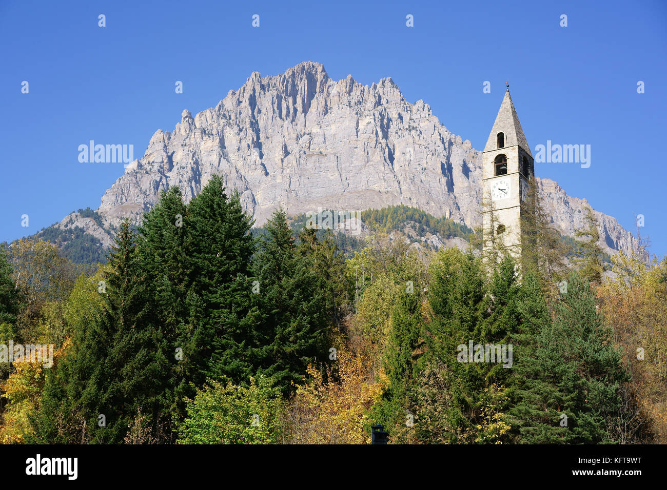 Glockenturm mit Herbstfarben im Vordergrund und einer massiven Klippe (Monte Bersaio) als Hintergrund. Sambuco, Provinz Cuneo, Piemont, Italien. Stockfoto