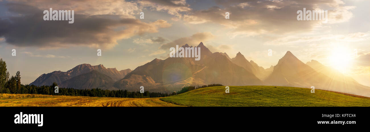 Ländlichen Gebieten in der Nähe der Tatra im Sommer bei Sonnenuntergang. schöne Panorama der landwirtschaftlichen Fläche. Wunderschöne Bergrücken mit hohen felsigen Gipfeln Stockfoto