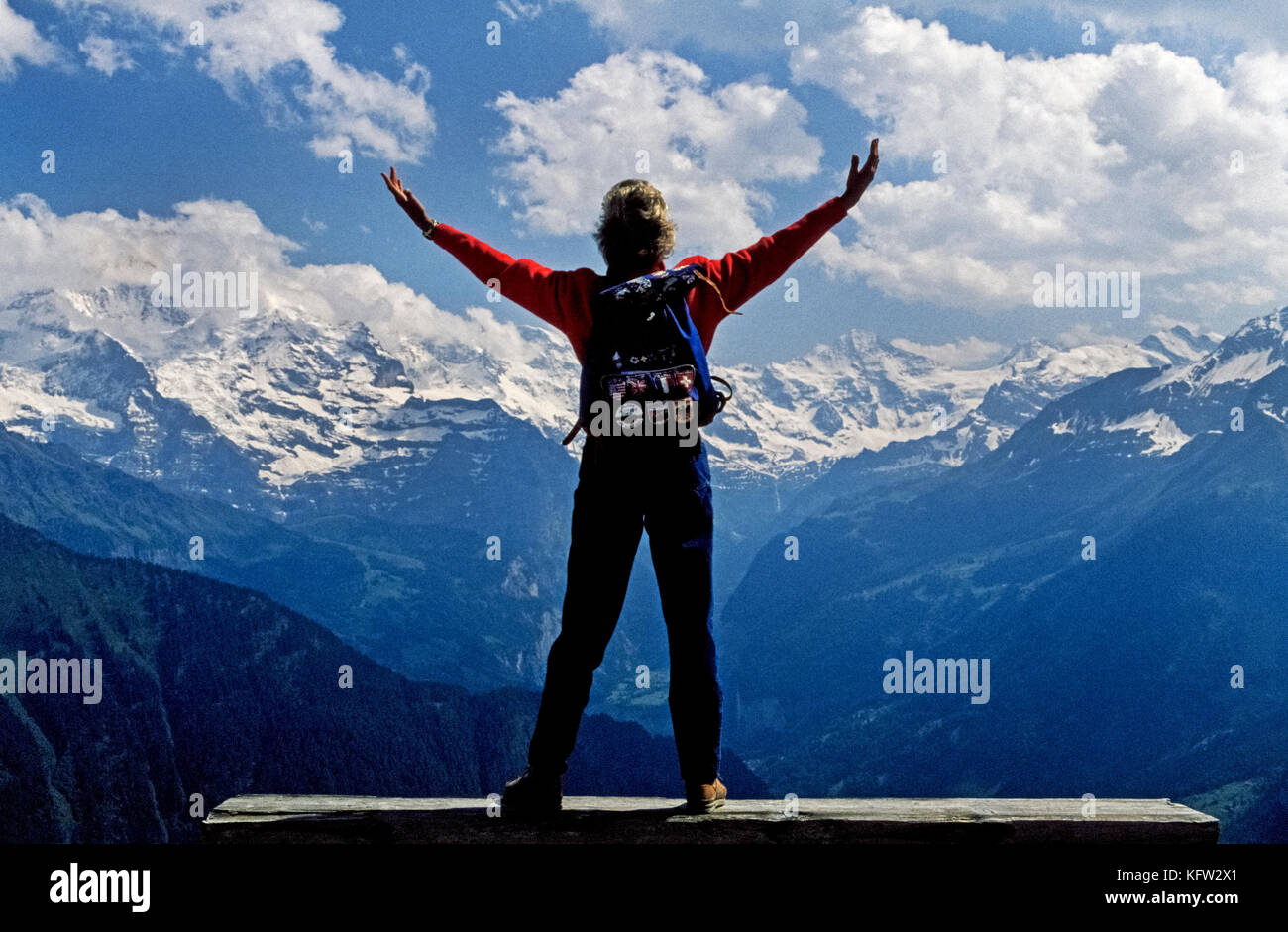 Eine weibliche Besucher an einem Tag - Wanderung wirft die Arme in Hochstimmung im Blick auf die Schweizer Alpen im Berner Oberland, einem beliebten Reiseziel südlich von Bern, der Hauptstadt der Schweiz. Die Region ist mit Wandern Wanderwege durchzogen, die dazu führen, dass wenig alpinen Dörfer und Panoramen von schneebedeckten Bergen. Stockfoto