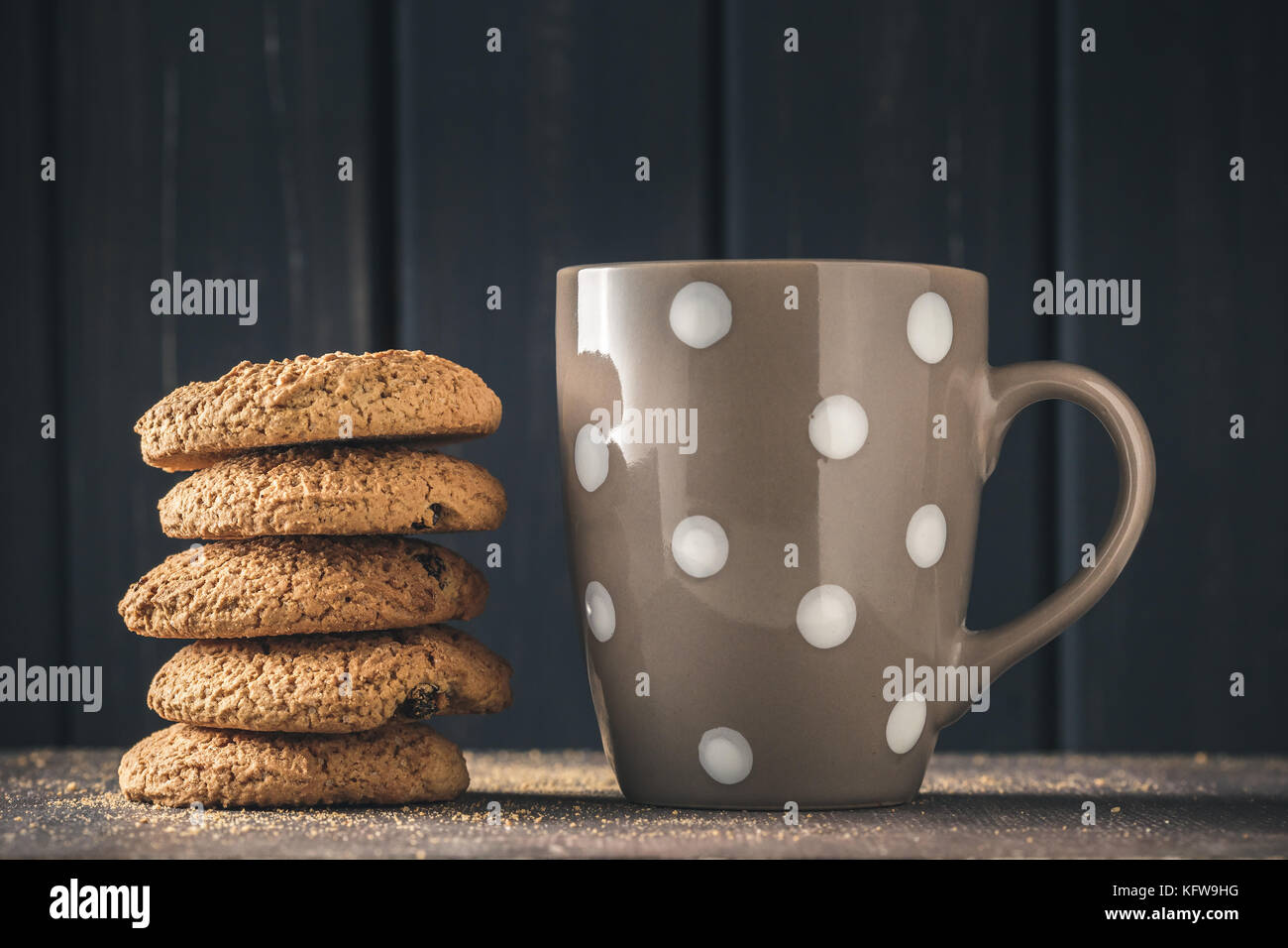 Stapel von oat Cookies und Polka Dot Becher mit heißem Getränk über dunklen Hintergrund Stockfoto