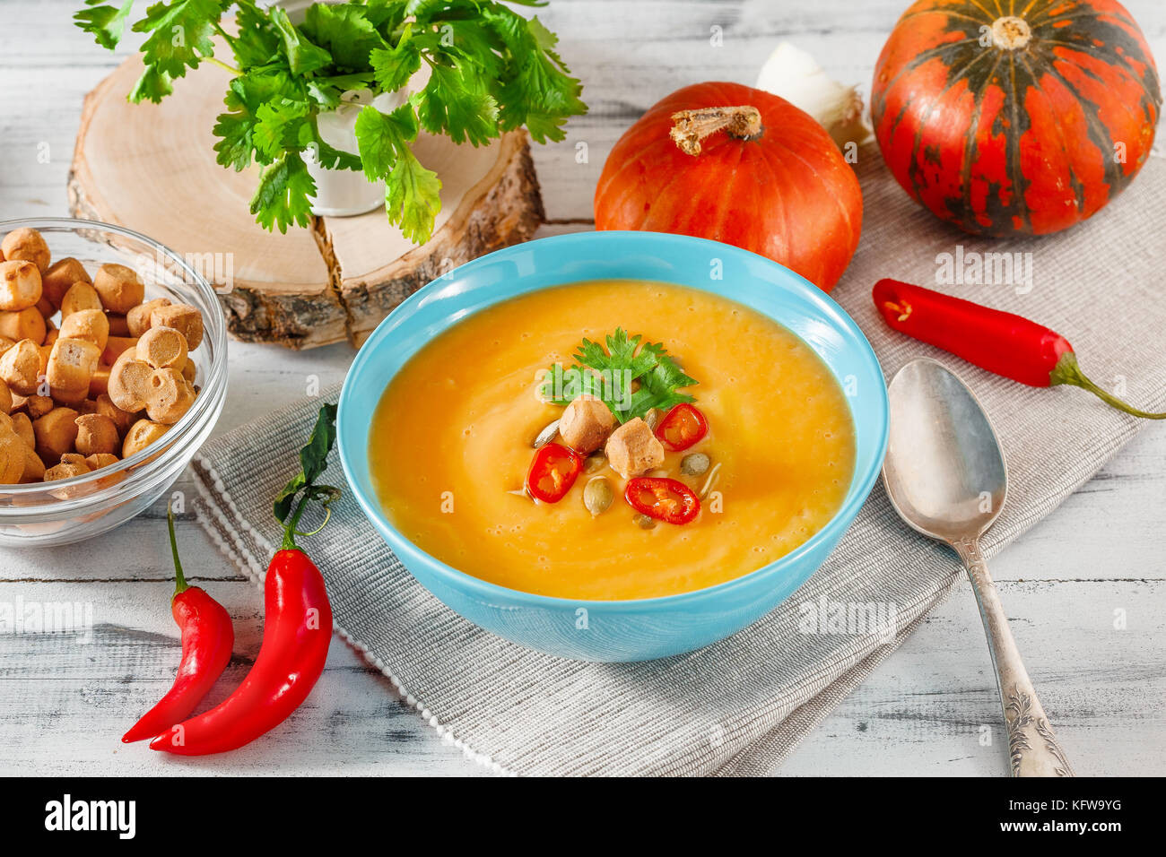 Kürbissuppe mit Chili, Kürbiskerne, Croutons und Petersilie in blaue Schale auf weißem Holz- Hintergrund Stockfoto
