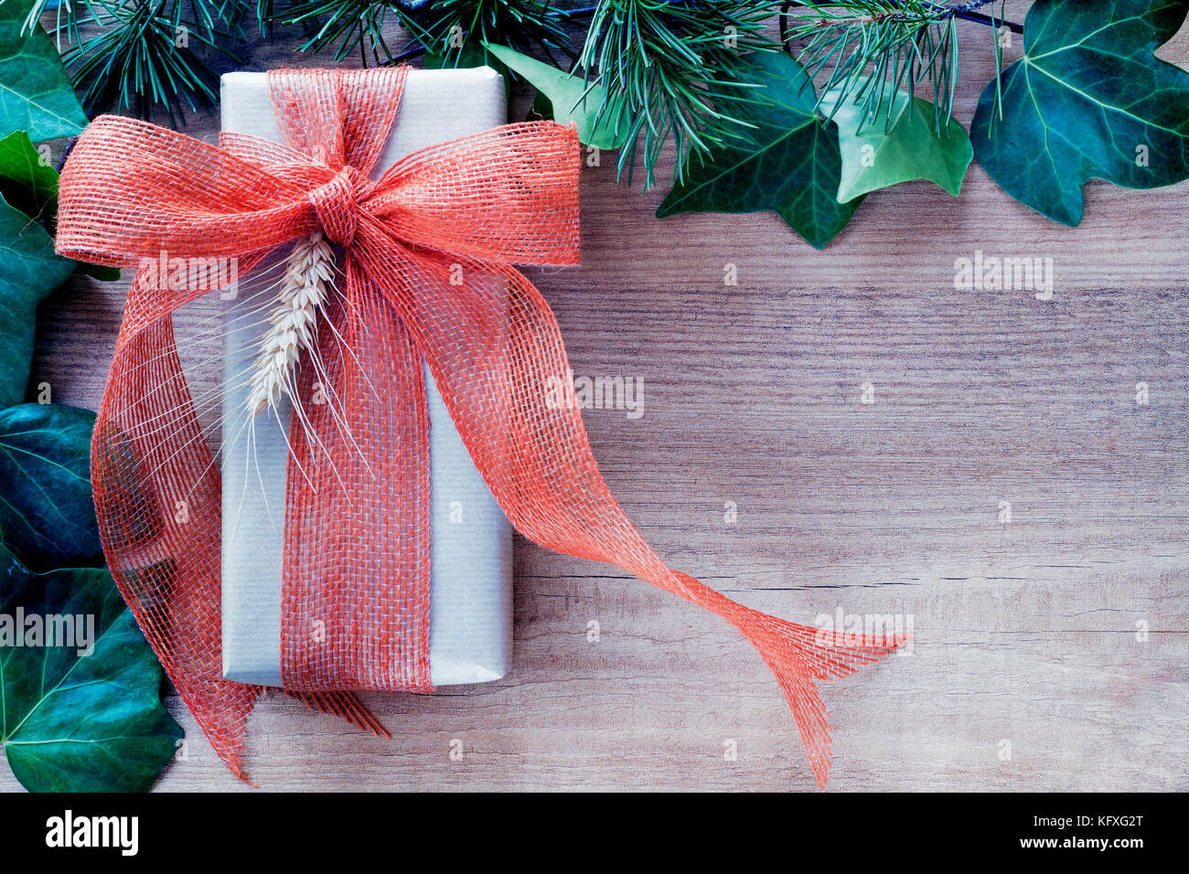 Verpackung im Landhausstil Geschenk mit Orange Ribbon und Zweig, mit Efeu Blätter auf Holz Hintergrund eingerahmt. nach oben anzeigen und kopieren. Stockfoto