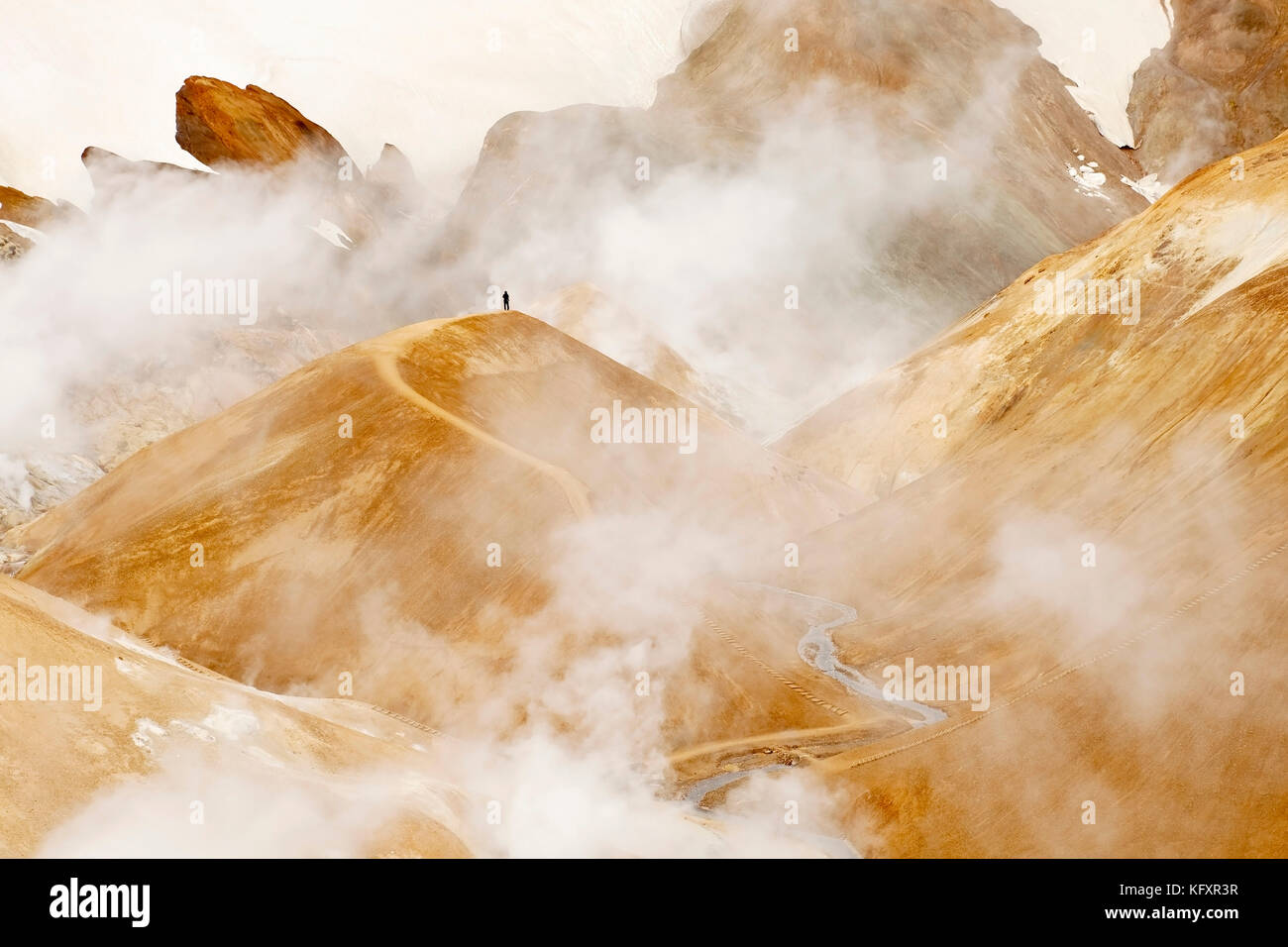 Ein Mensch im Hochtemperaturgebiet mit dampfenden heißen Quellen, Rhyolitbergen und Schnee, Hveradalir, Kerlingarfjöll Stockfoto