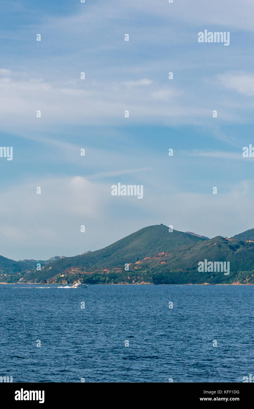 Vertikale Foto von einem Boot das Segeln im Mittelmeer. Das Boot vor der Küste mit paar Felsen der Berge in der Toskana Italien. Die Felsen sind ne Stockfoto