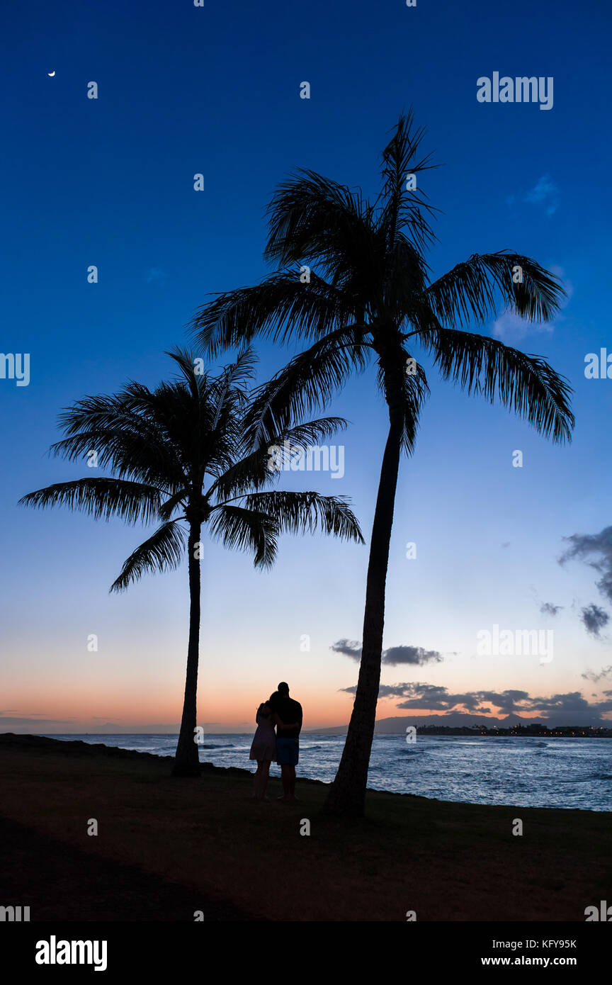 Silhouette von ein paar beobachten einen wunderschönen tropischen hawaiianischen Sonnenuntergang über dem Pazifischen Ozean in Magic Island auf Oahu, HI. Stockfoto