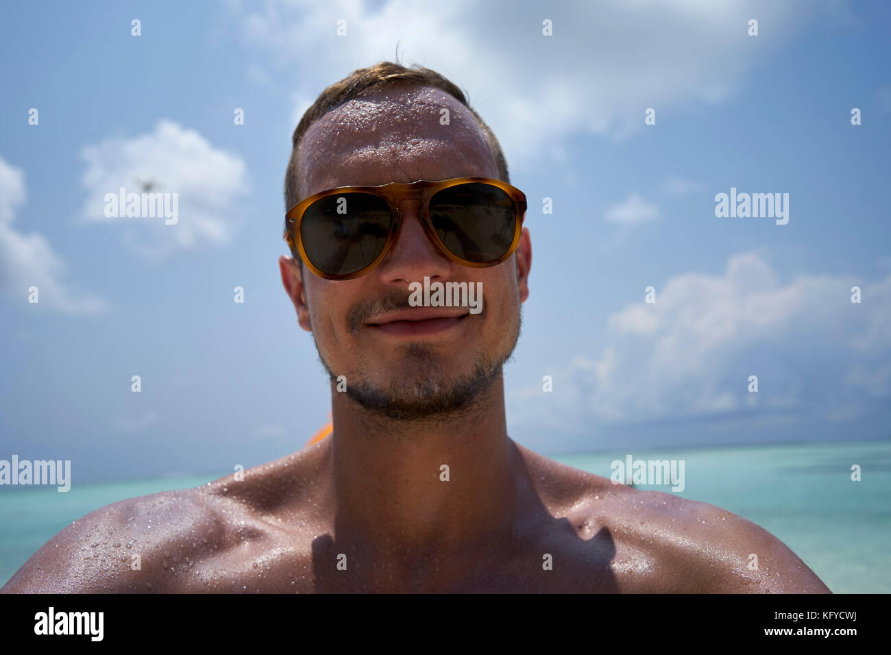 Mann mit kurzen Haaren, Bart und Sonnenbrille nimmt eine selfie am Strand Stockfoto