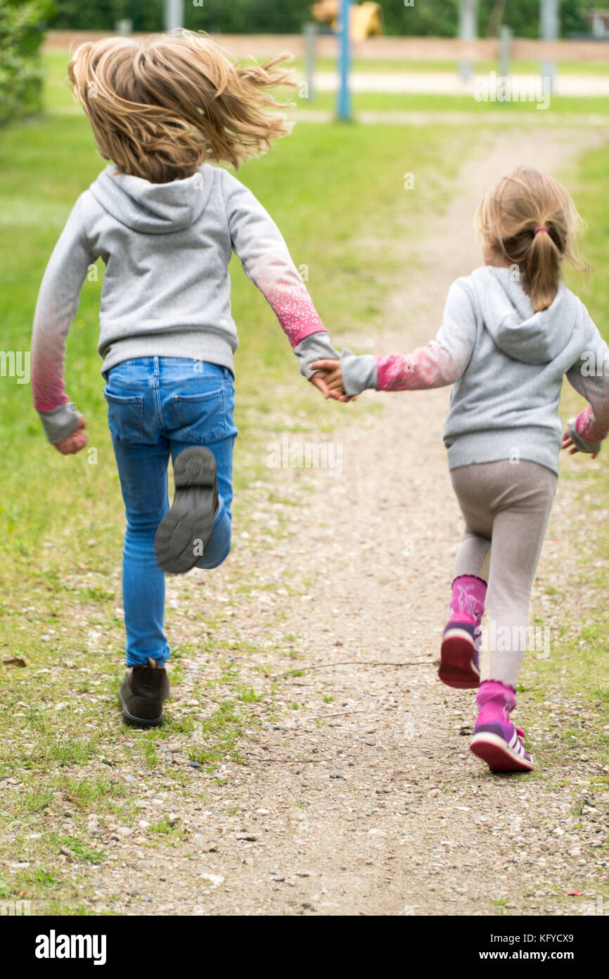 Zwei Mädchen laufen Hand in Hand über einen Sandweg Stockfoto