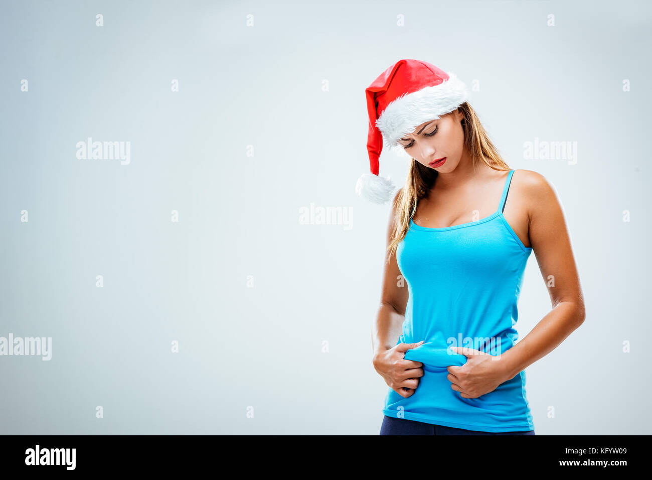 Freudlose Frau mit einem santa Mütze auf dem Kopf, kneifen Taille und prüfen Ihr Körperfett. weißen Hintergrund. Stockfoto