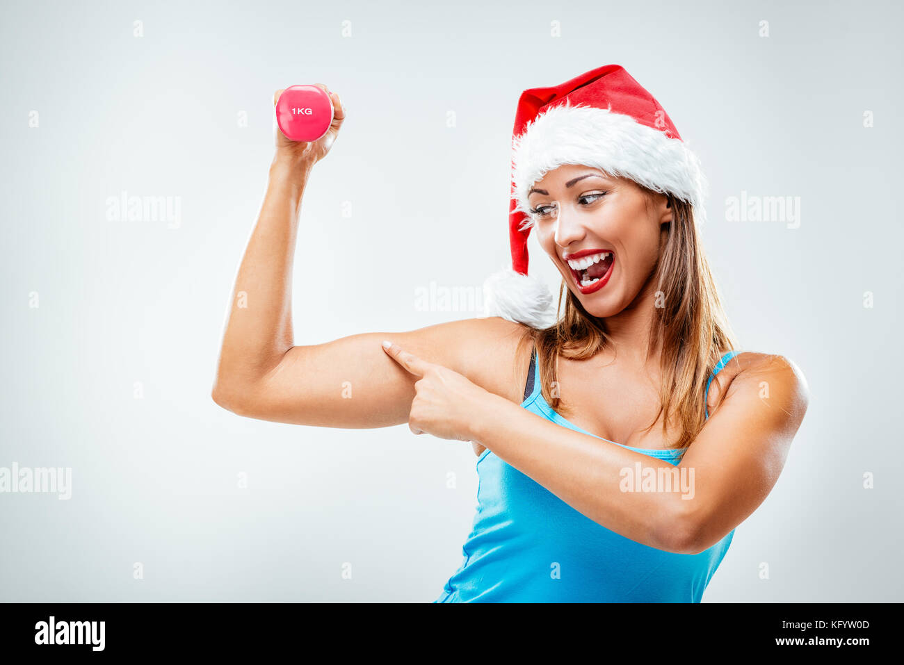 Fitness Mädchen lächelte glücklich mit einem santa Mütze auf dem Kopf, Gewichte zu heben suchen Krafttraining hand Muskeln. weißen Hintergrund. Stockfoto