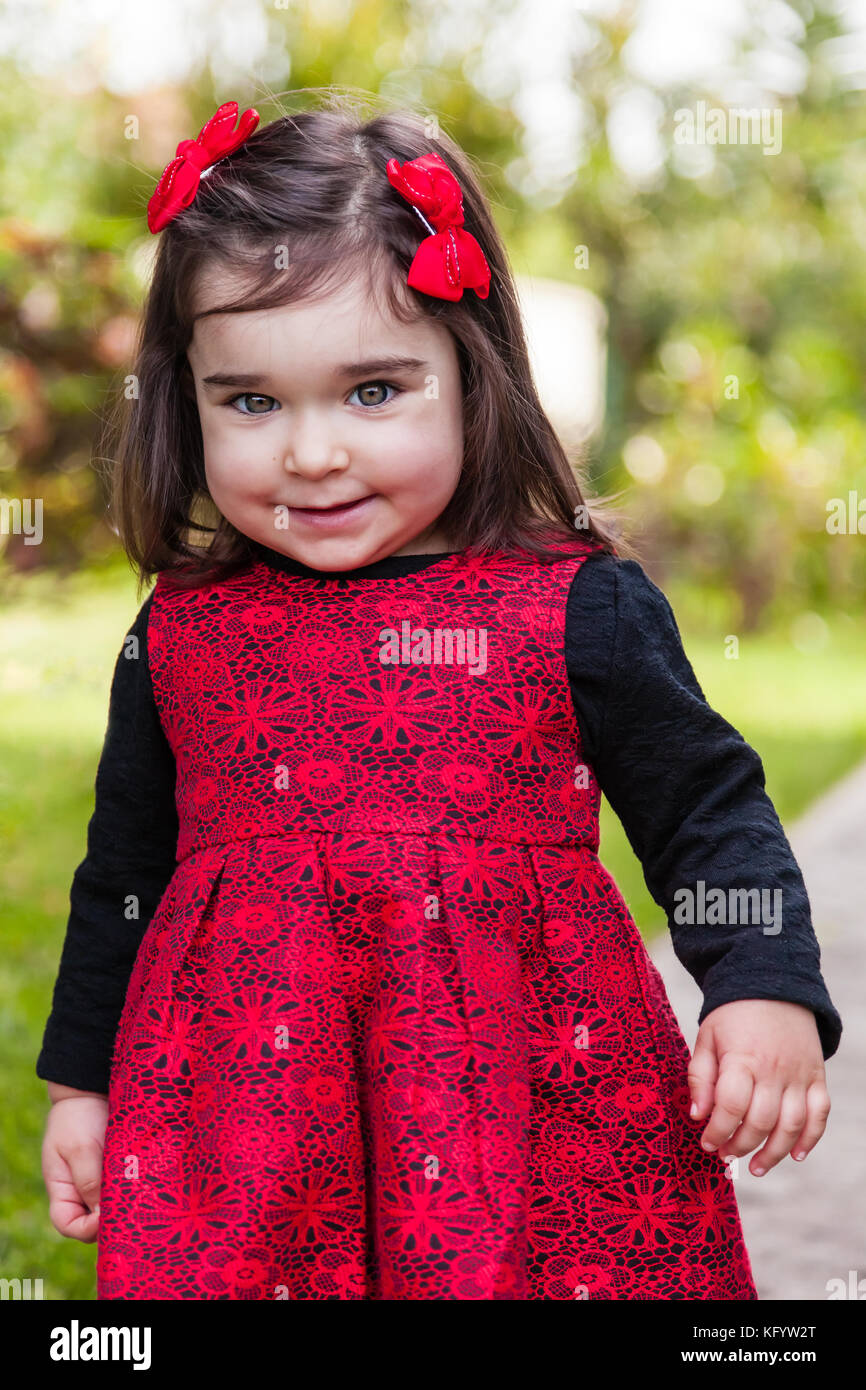 Niedlich, hübsch, fröhlich, lächelnd Kleinkind Baby Girl, mit einem frechen verspielten Lächeln mit eleganten roten und schwarzen Kleid. zehn Monate alt Stockfoto