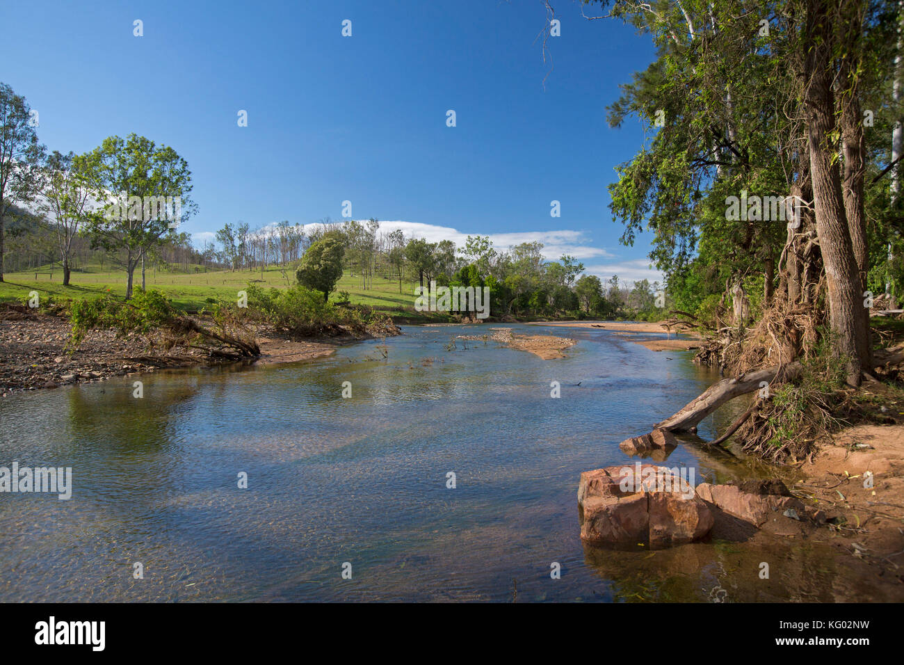 Bunte australische Landschaft mit flachen blauen Wassern des Boyne River von Wäldern und grünen und grasigen Hang unter blauem Himmel gesäumt Stockfoto