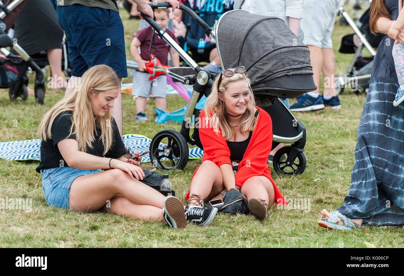 Zwei junge Frauen, die auf dem Boden sitzend an der Coventry Godiva Music Festival, Coventry, West Midlands, UK. Stockfoto