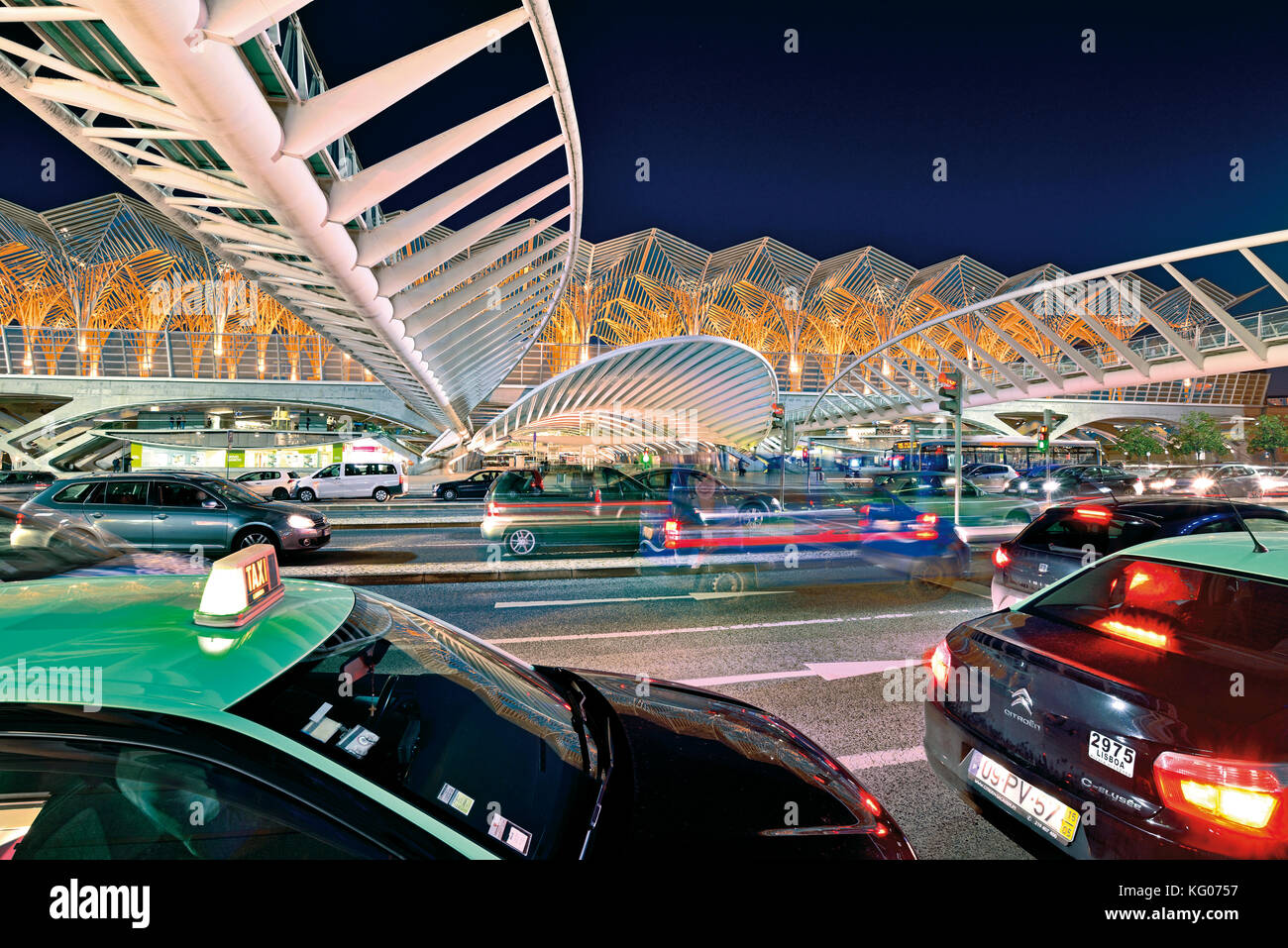 Autos und Taxis bewegen sich nachts vor futuristischer Stahldachkonstruktion Stockfoto