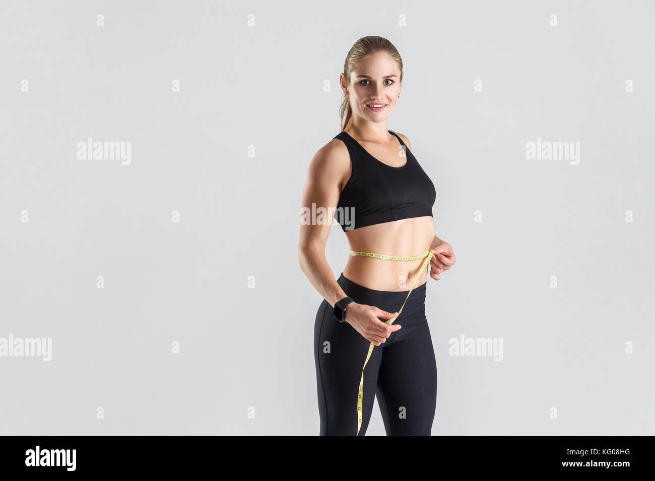 Gewicht Verlust Konzept. ideale Abbildung und Magen. Frau mit Zentimeter- und lächelnd. studio Shot, grauer Hintergrund Stockfoto