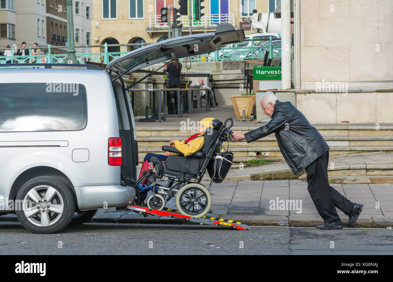 Mann drücken behindertes Kind in einen Rollstuhl, eine Rampe in ein Auto. Stockfoto