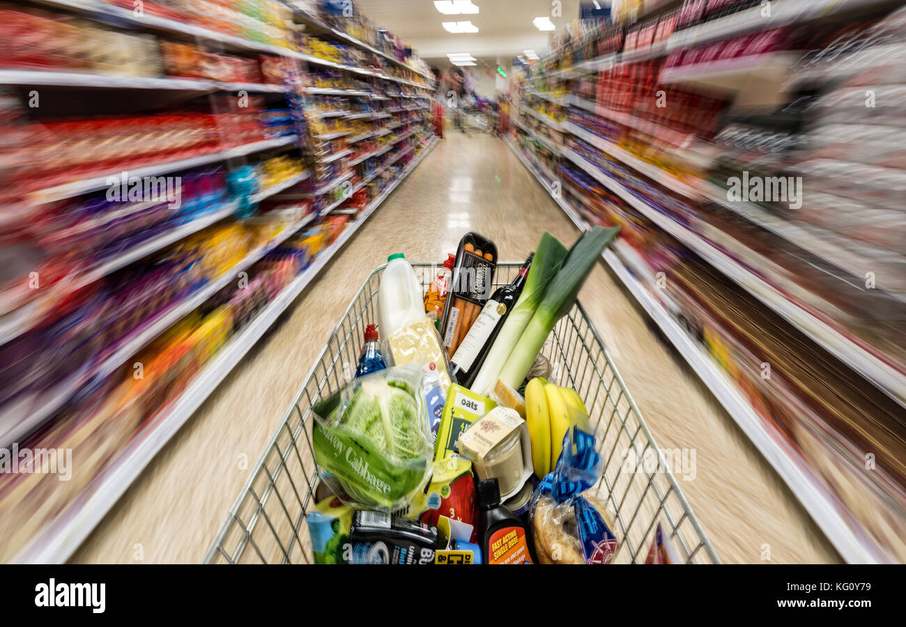 Einen Einkaufswagen mit Lebensmitteln beladen ist gesehen bewegt sich mit der Geschwindigkeit nach unten einen Supermarkt in Gang, in London, UK. Stockfoto