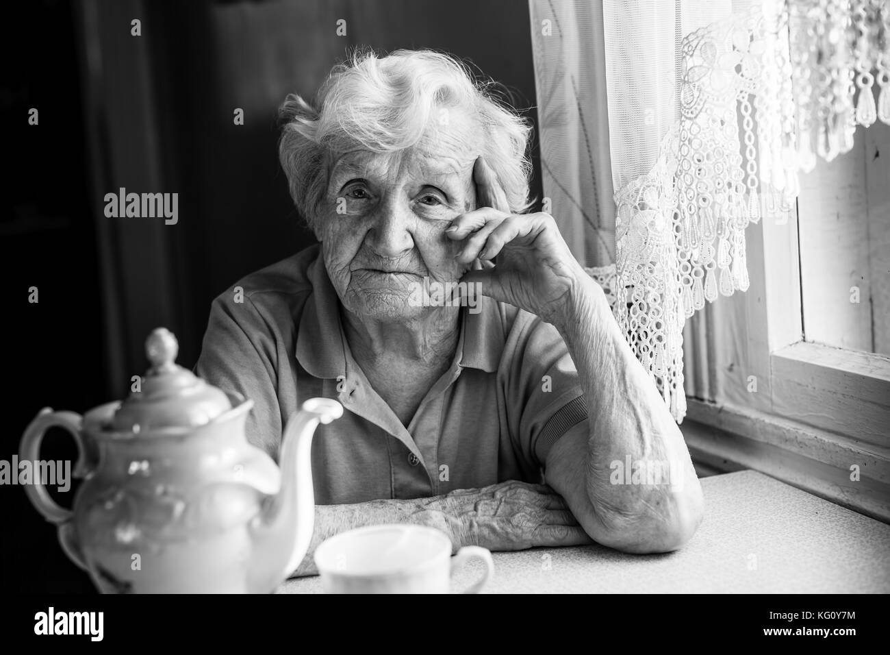 Portrait von einer älteren Frau an einem Tisch mit einer Kanne Tee. schwarz-weiß-Foto. Stockfoto
