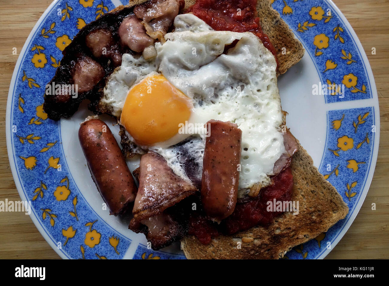 Frühstück mit geräuchertem Speck, Würstchen, Spiegeleier und Braun grunchy Toast Stockfoto