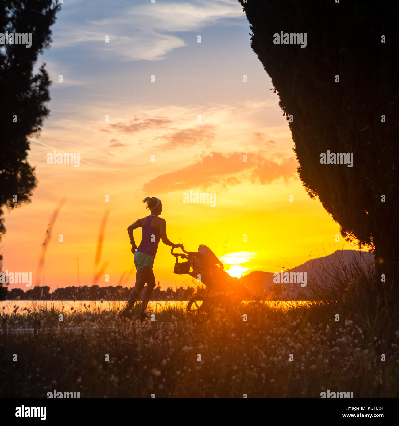 Mutter mit Kind im Kinderwagen genießen Mutterschaft bei Sonnenuntergang und Berge Landschaft laufen. Jogging oder Power walking Frau mit Kinderwagen an einem Strand im su Stockfoto