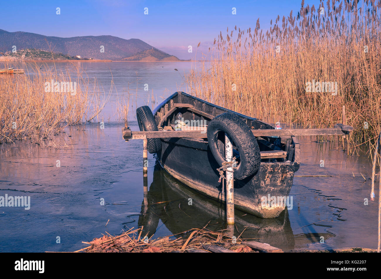 Fischerboot aus Schilf spiegelt sich auf dem gefrorenen Wasser Der prespa See umgeben. Stockfoto