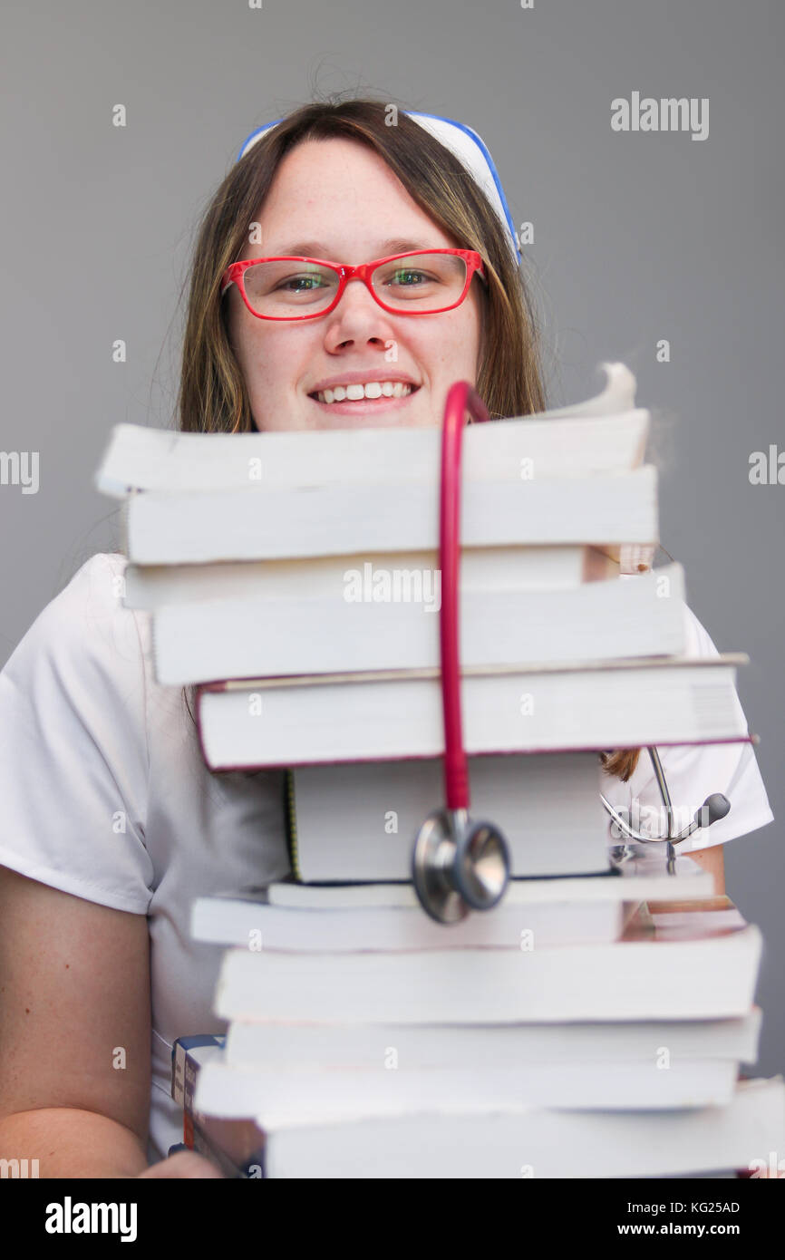 Junge weibliche Krankenschwester student Portrait tragen weiße Kittel, cap Holding groß der Krankenpflege Lehrbücher Stapel Stockfoto