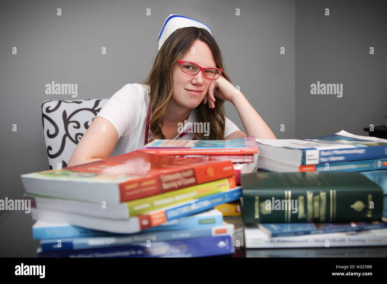 Junge gelangweilt und weiblichen Krankenschwester portrait tragen weiße Kittel, Kappe mit Krankenpflege Lehrbücher auf dem Tisch müde Stockfoto