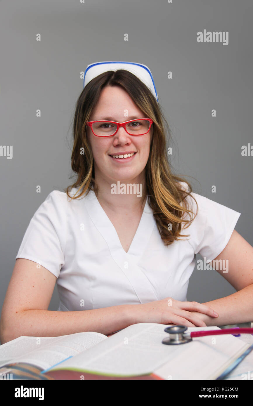 Junge weibliche Krankenschwester portrait tragen weiße Kittel, Kappe mit Krankenpflege Lehrbücher auf den Tisch und lächelte, Stockfoto