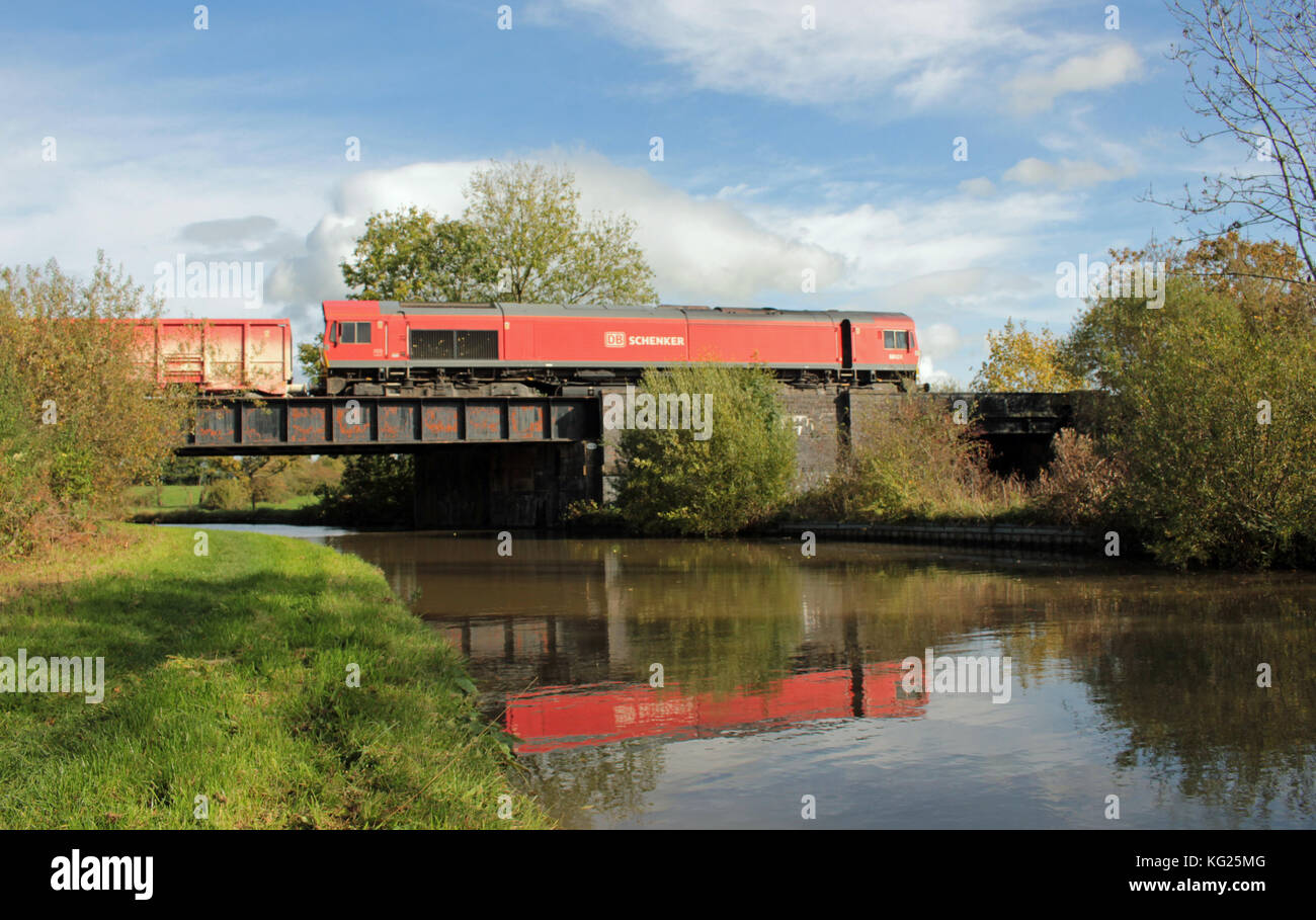 Eine rote Güterlokomotive und ihr Zug spiegeln sich in den Gewässern des Trent- und Mersey-Kanals wider, wenn sie ihn in der Nähe von Middlewich in Cheshire kreuzt. Stockfoto