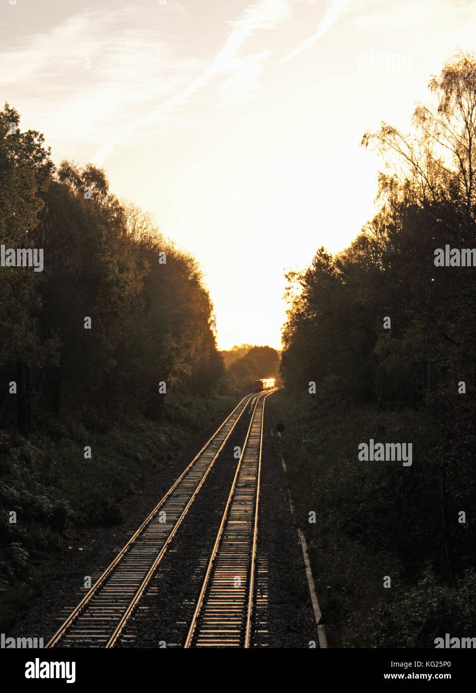 Am frühen Morgen fährt ein Zug entlang der Gleise und die Schlafenden werden von der aufgehenden Sonne beleuchtet, da er um eine Kurve verschwindet. Stockfoto