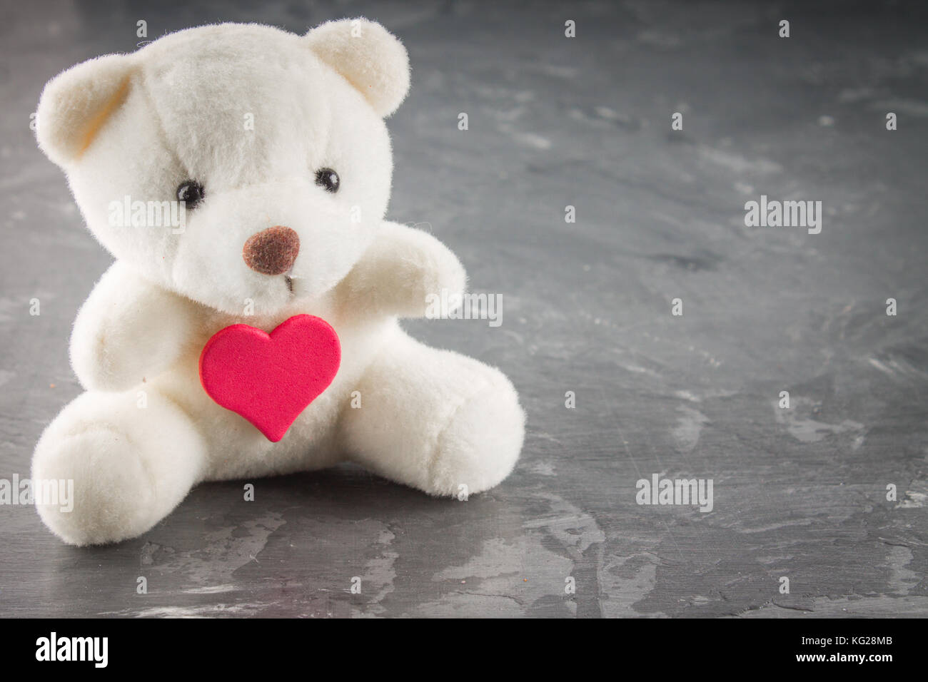 Weißer Teddybär mit Liebesbrief auf roten Herzen auf grauen Hintergrund