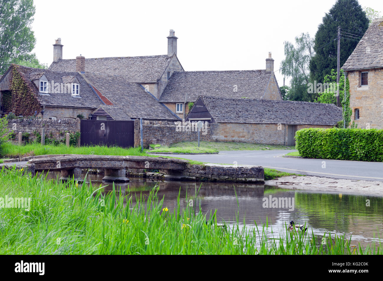 Traditionelle Häuser aus Stein, die von einem Fluss mit einer kleinen Brücke, in ländlichen Cotswolds Dorf. Stockfoto