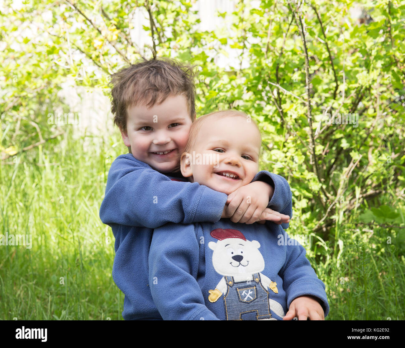 Zwei glückliche kleine Brüder spielen im Freien im Sommer. Der ältere Bruder umarmt Jungen Stockfoto