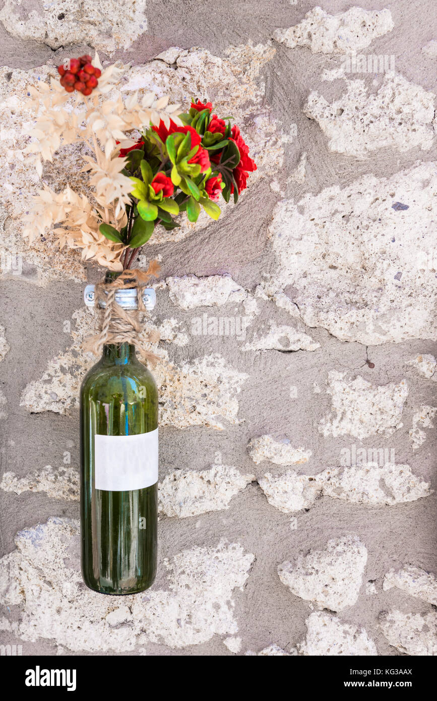 Leere grüne Weinflasche mit Blumen innen auf weißer Steinwand zur Dekoration in Alacati Stadt, Türkei. Kopierbereich Stockfotografie