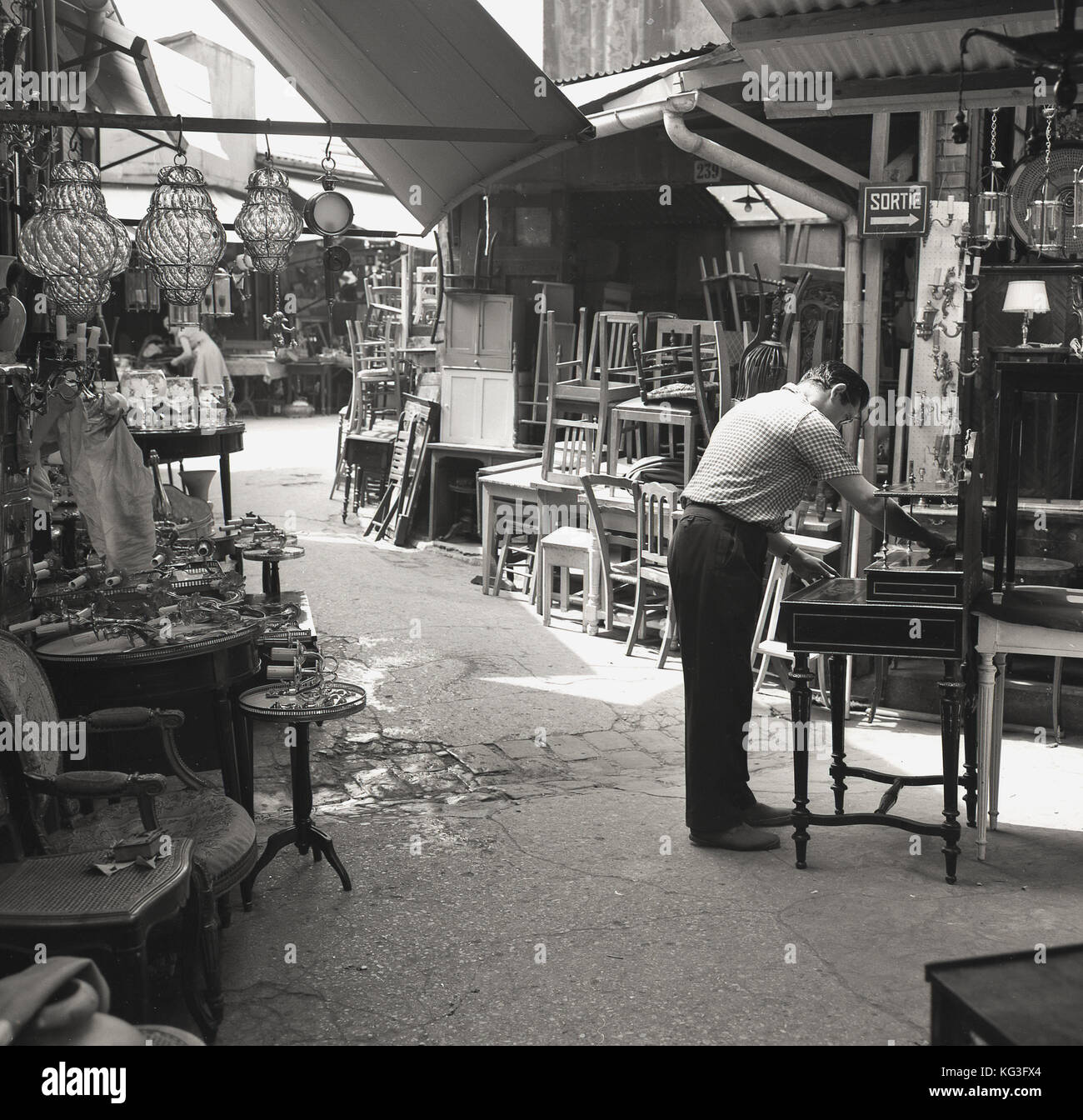 1950s, historisch, ein Stallholder, der Möbel in einem Durchgang an einem der berühmten Pariser Puces putzt, Flohmärkte, die alles von antiken Möbeln bis zu Vintage Bric-a-brac, Paris, Frankreich, zum Verkauf haben. Stockfoto