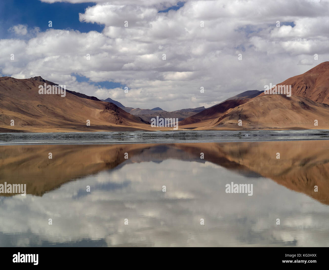 Spiegelbild im Wasser des Grates, auf der Oberfläche des Sees spiegeln die braunen Hügeln, der graue Streifen an der Küste und der Himmel mit Cumulus Stockfoto