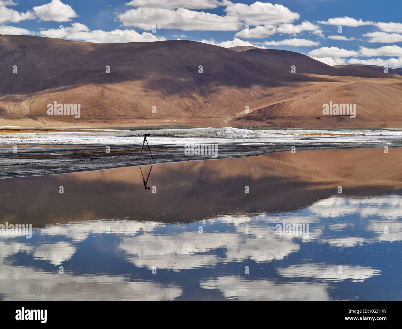 Mountain Lake, auf eine ruhige Wasseroberfläche Spiegel braune Hügel und der Himmel mit Wolken, auf einem sandigen Landzunge gibt es ein Stativ mit Kamera, der Himalaja, Stockfoto