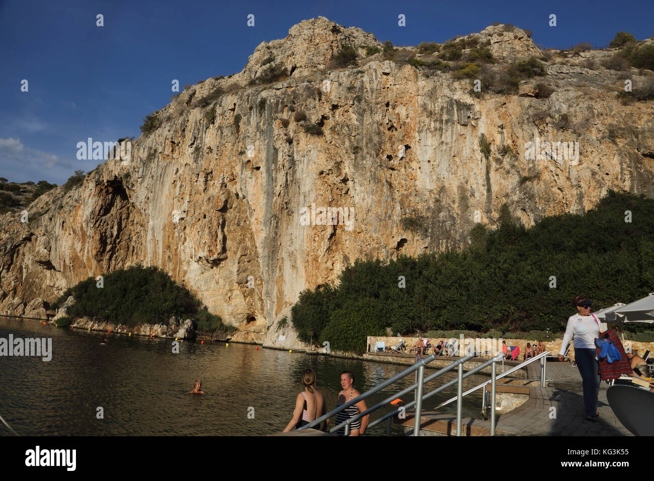 Vouliagmeni Athen Griechenland Touristen, die im Vouliagmeni-See schwimmen, ein Naturbad - war einst eine Höhle, aber das Höhlendach fiel durch Erosion durch die hohe Temperatur des fließenden Wassers ein. Stockfoto