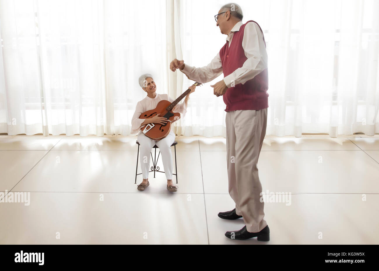 Ältere Frau spielt Gitarre und der ältere Mann tanzen Stockfoto