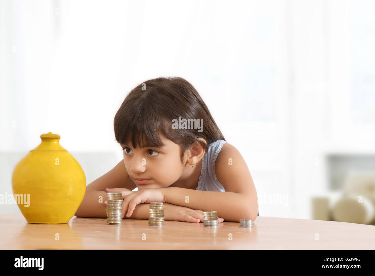 Mädchen lehnte sich auf Tisch bei piggy Bank suchen und Stapel von Münzen Stockfoto