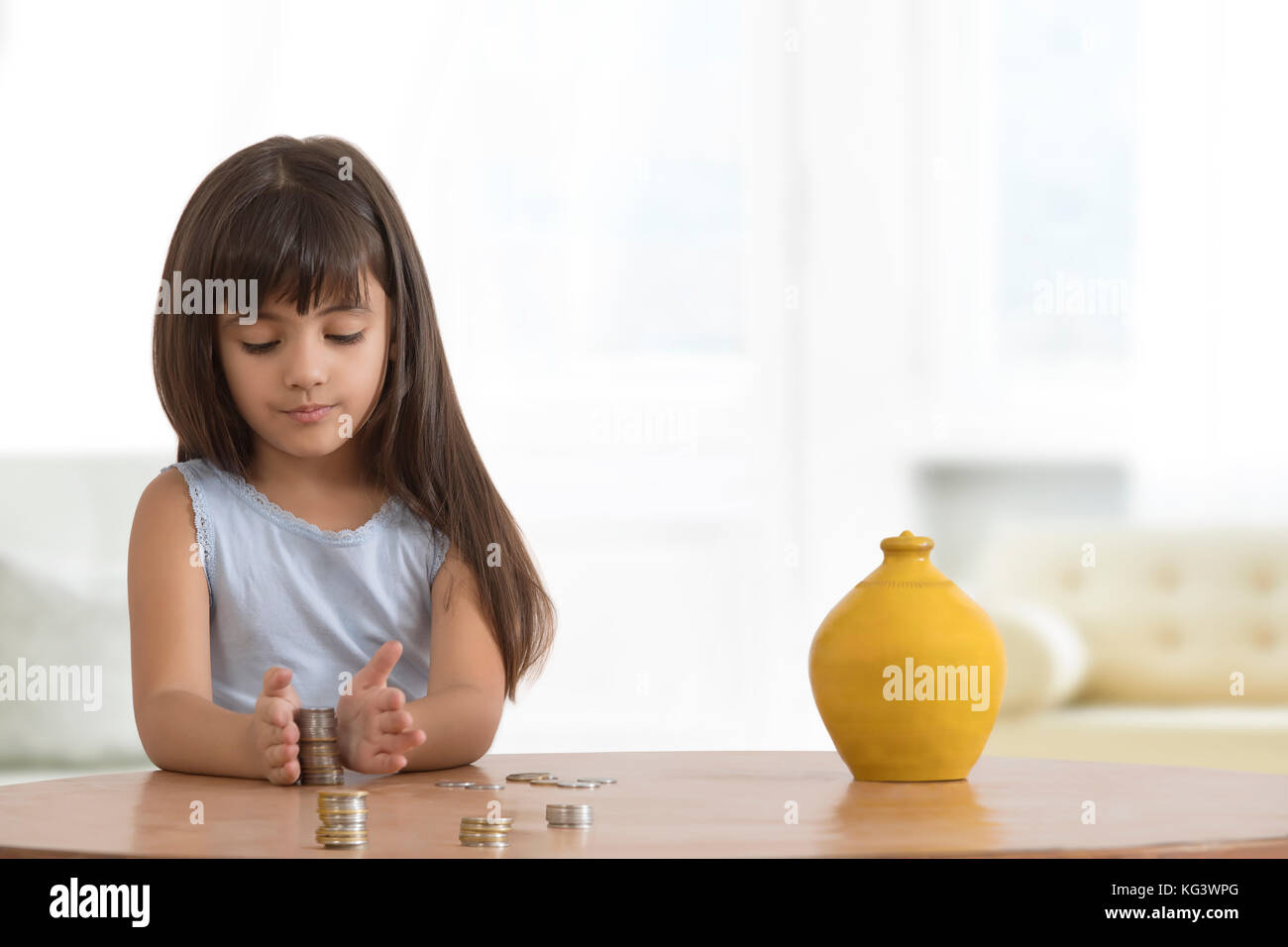 Mädchen, die die Münzen auf Tabelle mit Lehm piggy Bank Stockfoto