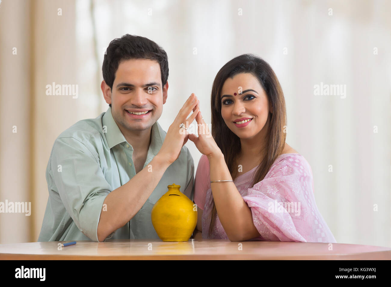 Der Mann und die Frau sitzen zusammen am Tisch mit Sparschwein Stockfoto