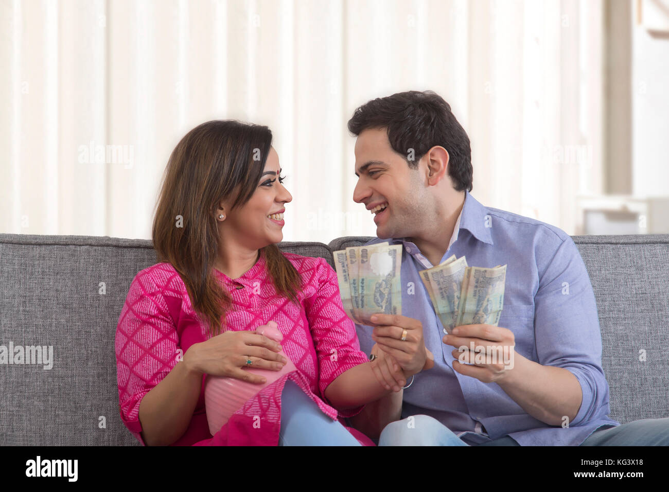 Glückliches Paar hält indische Währung und Lehm piggy Bank Stockfoto