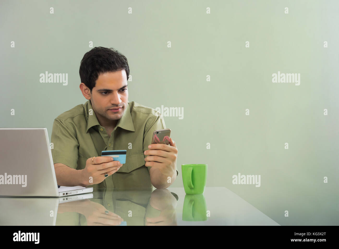 Mann online Einkaufen von Mobiltelefon und Kreditkarte am Tisch sitzt mit Laptop Stockfoto