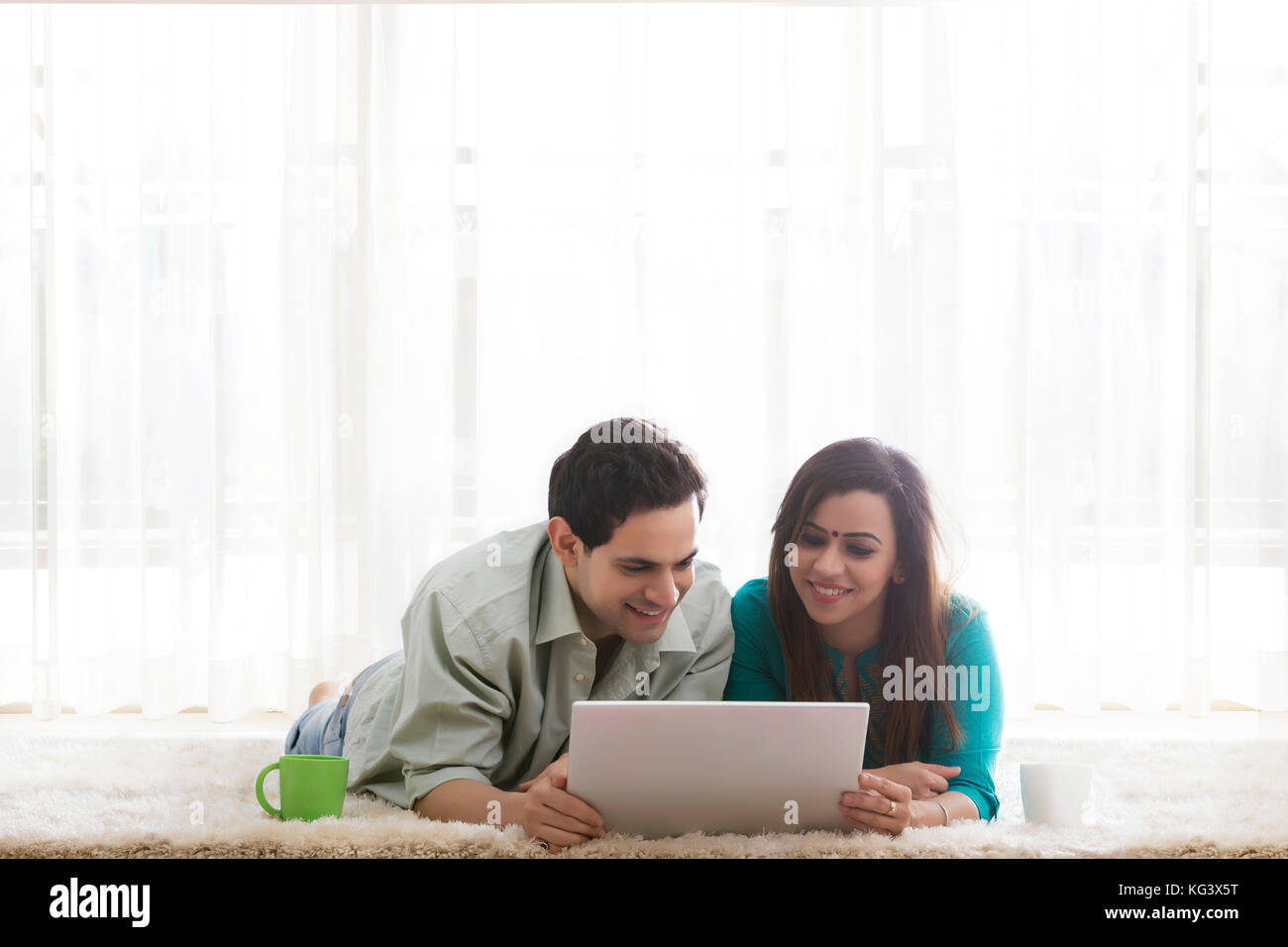 Paar auf dem Boden liegend mit Laptop und Kaffeetassen Stockfoto