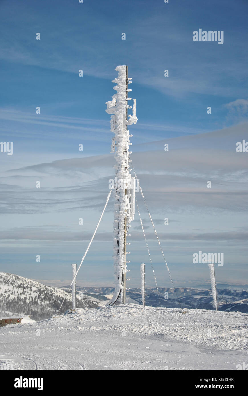 Telekommunikation Antenne auf der Spitze des Berges, gefroren und vollständig durch Schnee und Eiszapfen gegen den blauen Himmel mit einigen hohen Wolken bedeckt Stockfoto
