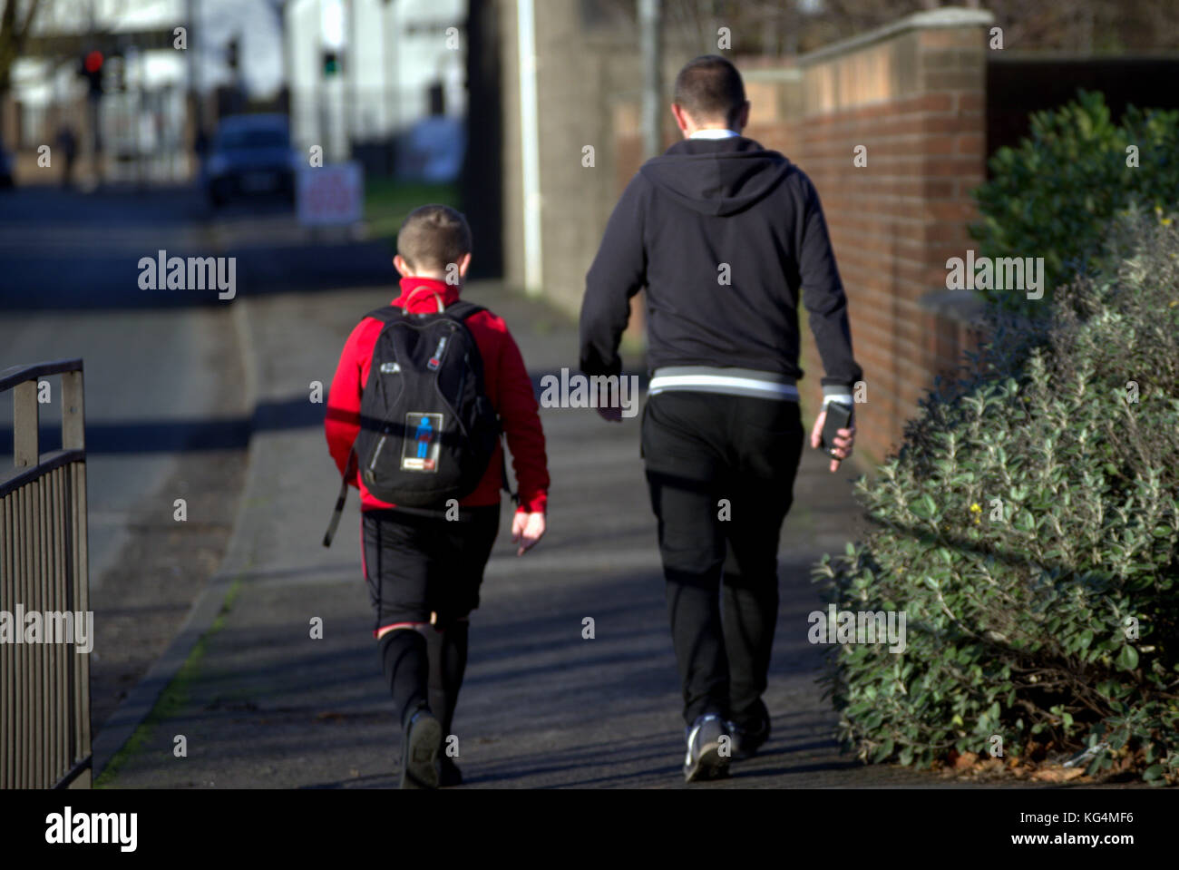 Vater und Sohn in Sportkleidung zu Fuß von der Schule nach Hause entlang der Straße in drumchapel in der Perspektive mit Rucksack aus gesehen hinter Stockfoto